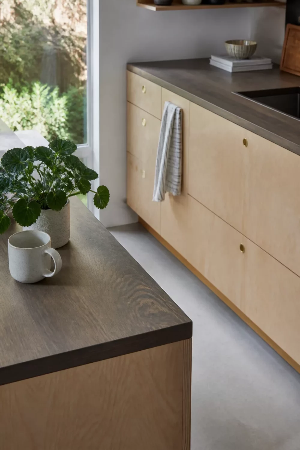 Fumed oak-look faux wood kitchen countertop on a Scandi island with blonde plywood cabinets and brass pulls