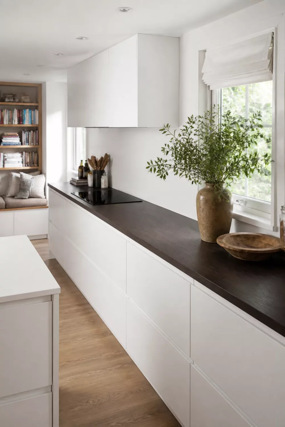 Ebonized faux wood kitchen countertops on white handleless cabinets with natural light and greenery styling.