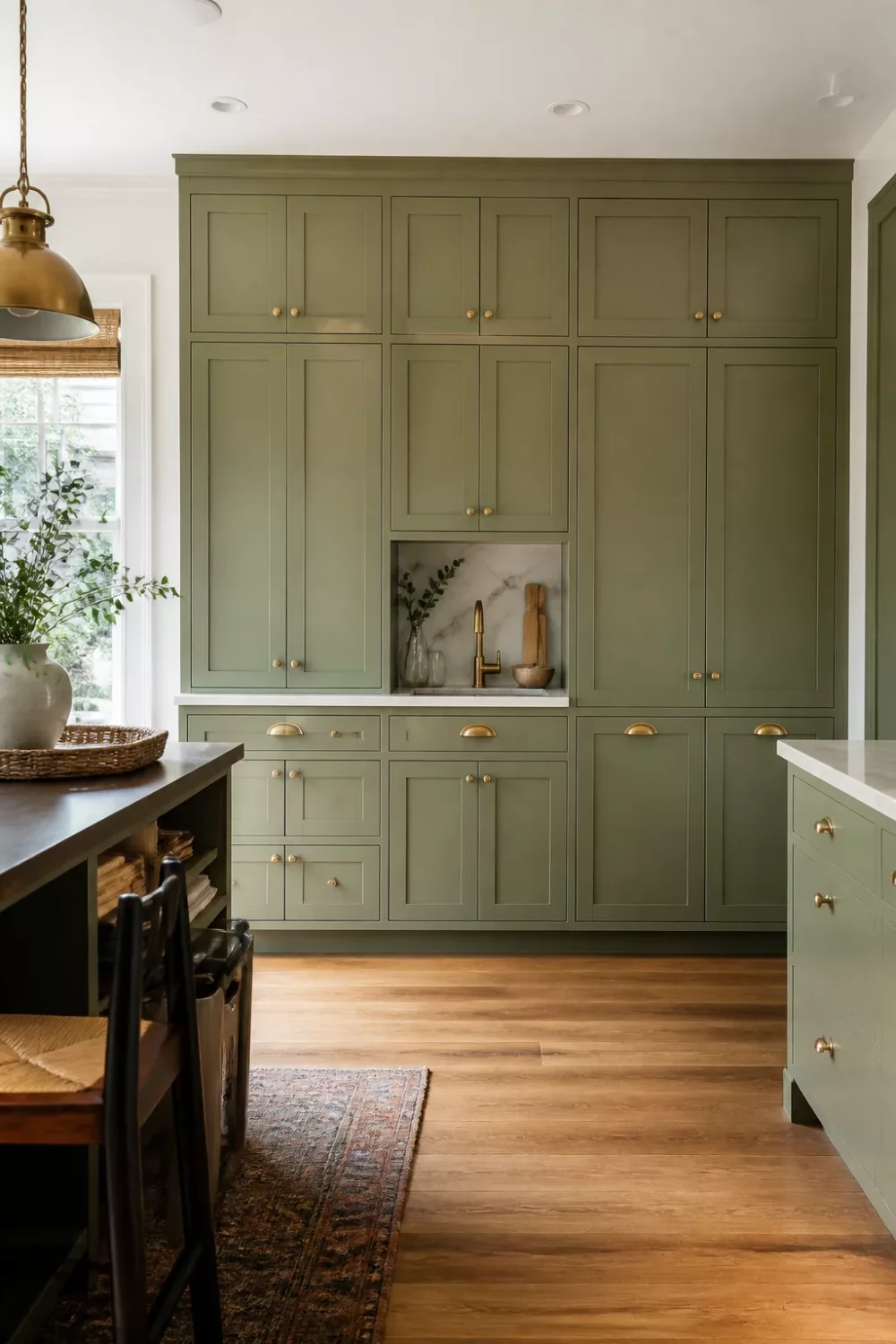 Floor-to-ceiling sage green kitchen cabinets with gold bin pulls, marble nook, and warm oak floors
