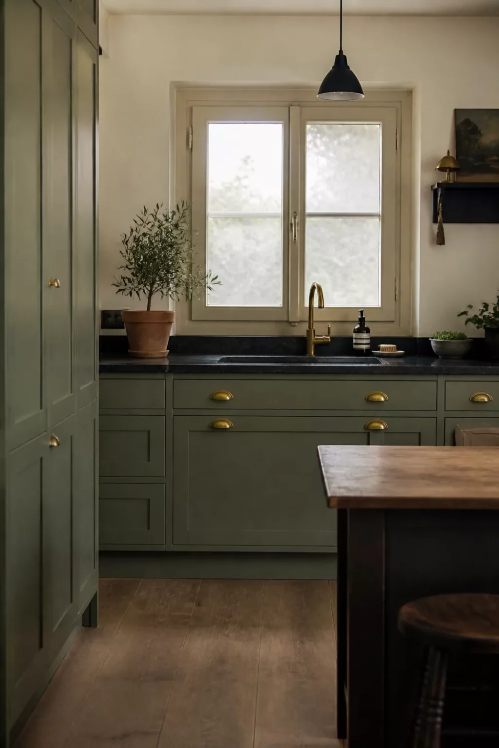 Sage green kitchen cabinets with gold cup pulls and black stone countertops — deep olive tones with aged brass hardware