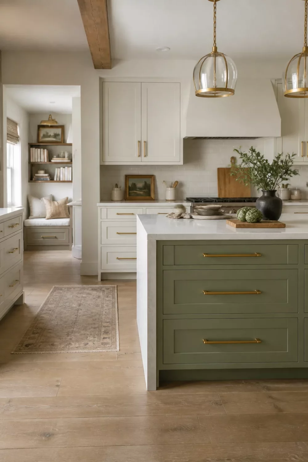 Open-plan sage green kitchen with brass handles, cream upper cabinets, exposed timber beams, and oak floors