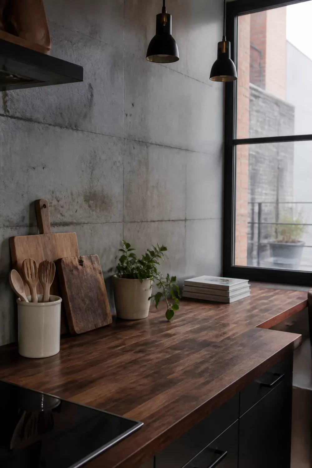 Dark walnut butcher block kitchen countertop paired with raw concrete backsplash and black pendant lights