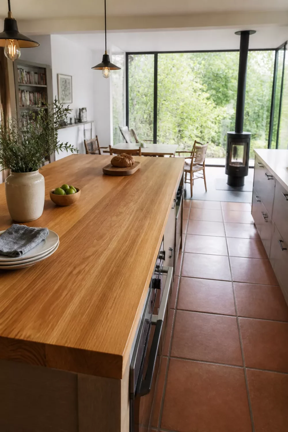 Solid oak wood kitchen countertop on island with terracotta tile floor and wood-burning stove in background